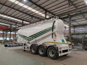 Rear view of 3 axle white dry bulk cement semi trailer with discharge hoses