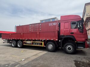 Side view of SINOTRUK HOWO 8x4 cargo truck with high roof cabin and red dropside cargo body