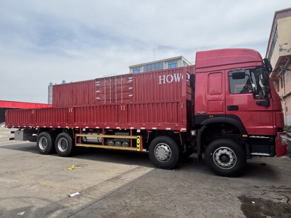 Side view of SINOTRUK HOWO 8x4 cargo truck with high roof cabin and red dropside cargo body